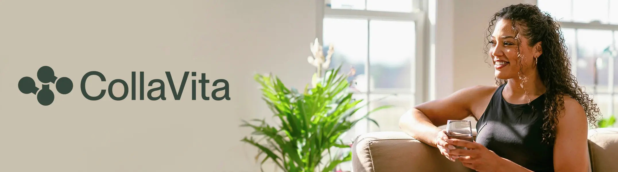 A smiling woman with curly hair enjoying a glass of water while sitting on a couch, next to the CollaVita logo, in a bright and plant-filled living room.